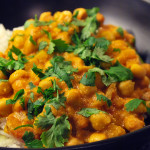 Svart tallrik fylld med en currygryta med kikärtor och jordnötter
